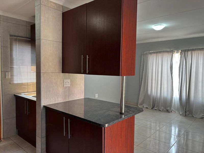 Open plan kitchen area featuring dark wood cabinetry, granite countertops, and tiled flooring, seamlessly flowing into the adjacent living space.