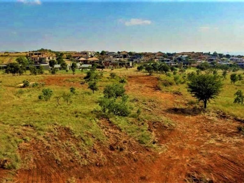 An aerial view of a vacant residential plot featuring natural terrain and vegetation with surrounding neighborhood development in the background.