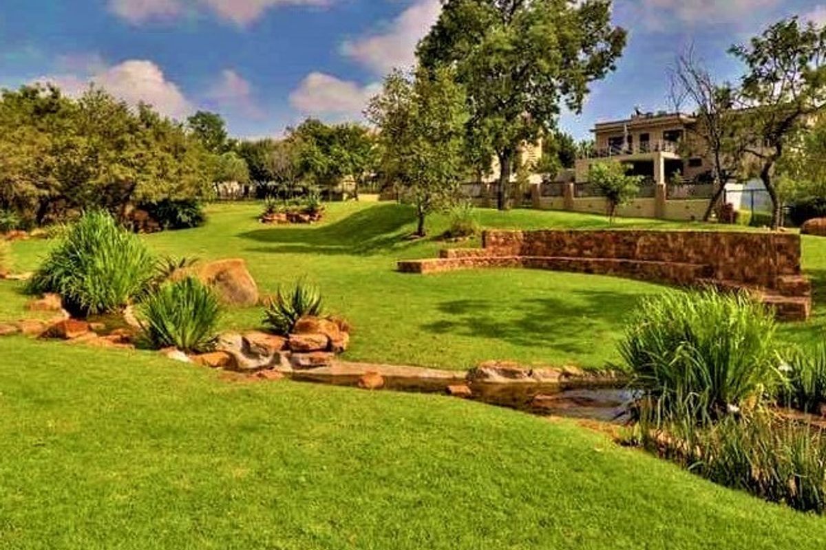 A well-maintained residential garden featuring a landscaped lawn, stone retaining wall, and a naturalistic water feature.