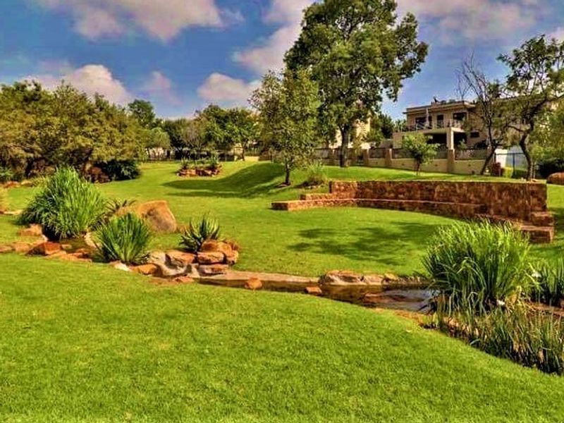 A well-maintained residential garden featuring a landscaped lawn, stone retaining wall, and a naturalistic water feature.
