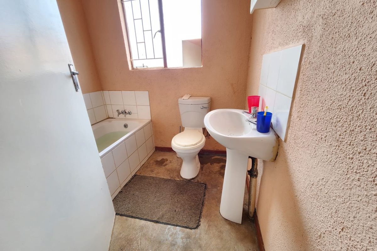 A compact bathroom featuring a bathtub, pedestal basin, and toilet, with textured walls and a concrete floor, requiring cosmetic updates and maintenance.