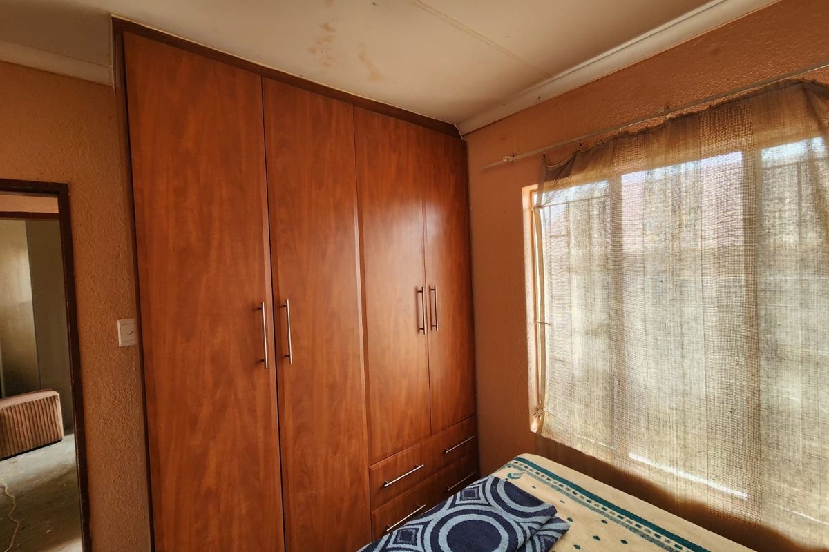 A bedroom featuring a large built-in wooden wardrobe and a window, showing visible signs of water damage on the ceiling.