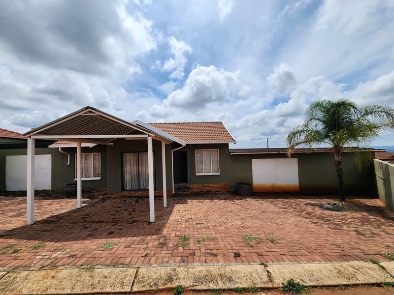 Front exterior view of a single-story house featuring a paved driveway, attached carport, and a tiled roof with a private boundary wall.