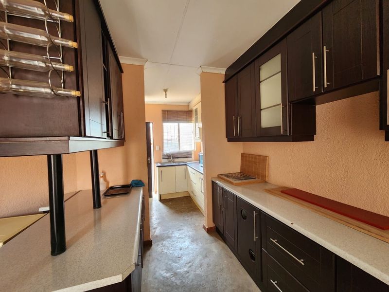 A galley-style kitchen featuring dark wood cabinetry, laminate countertops, and a functional layout with a secondary prep area near the window.