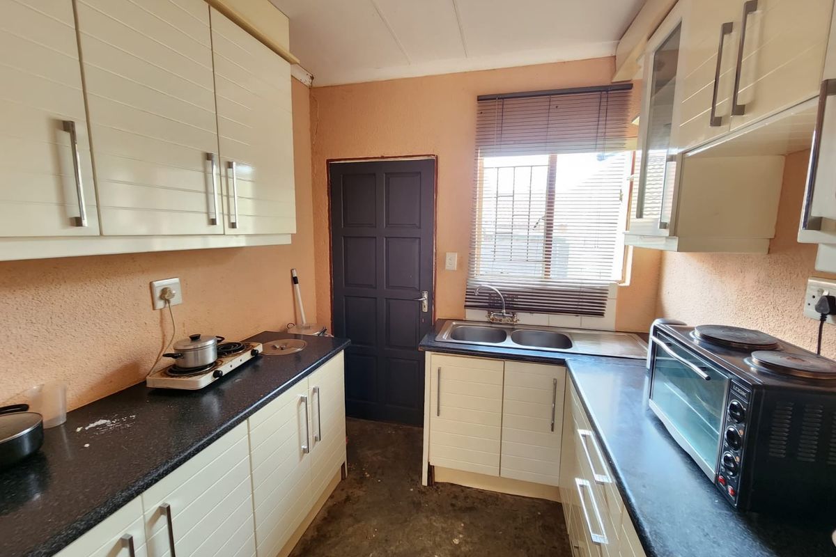 Compact kitchen featuring white built-in cabinetry, dark laminate countertops, double sink, and security bars on the window.