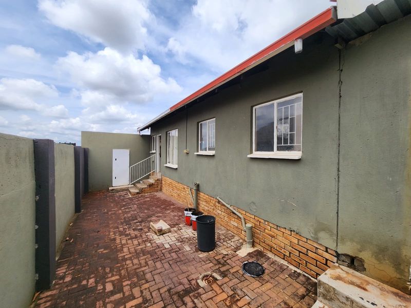 Rear exterior view of the property featuring brick paving, boundary wall, and external wall finishes with visible signs of wear.
