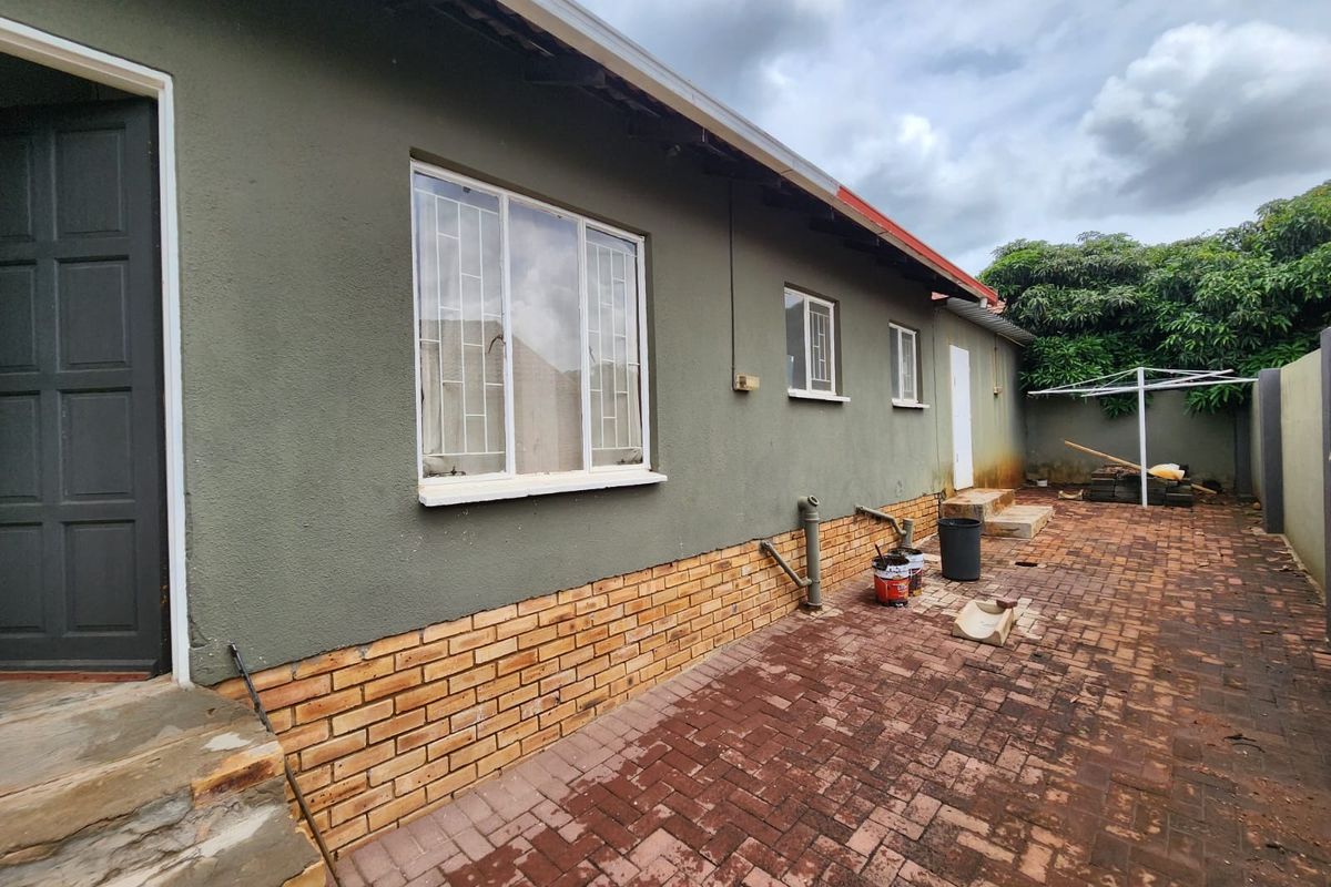 Rear exterior view of the property featuring brick paving, plastered walls with a brick plinth, and security bars on the windows.