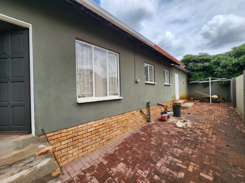 Rear exterior view of the property featuring brick paving, plastered walls with a brick plinth, and security bars on the windows.