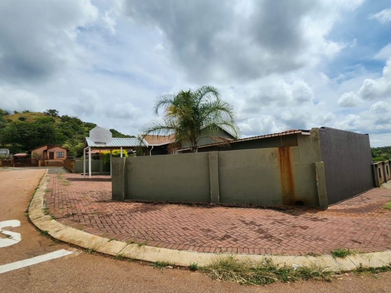 Exterior view of the property featuring a paved driveway, perimeter wall with visible staining, and a covered carport area.