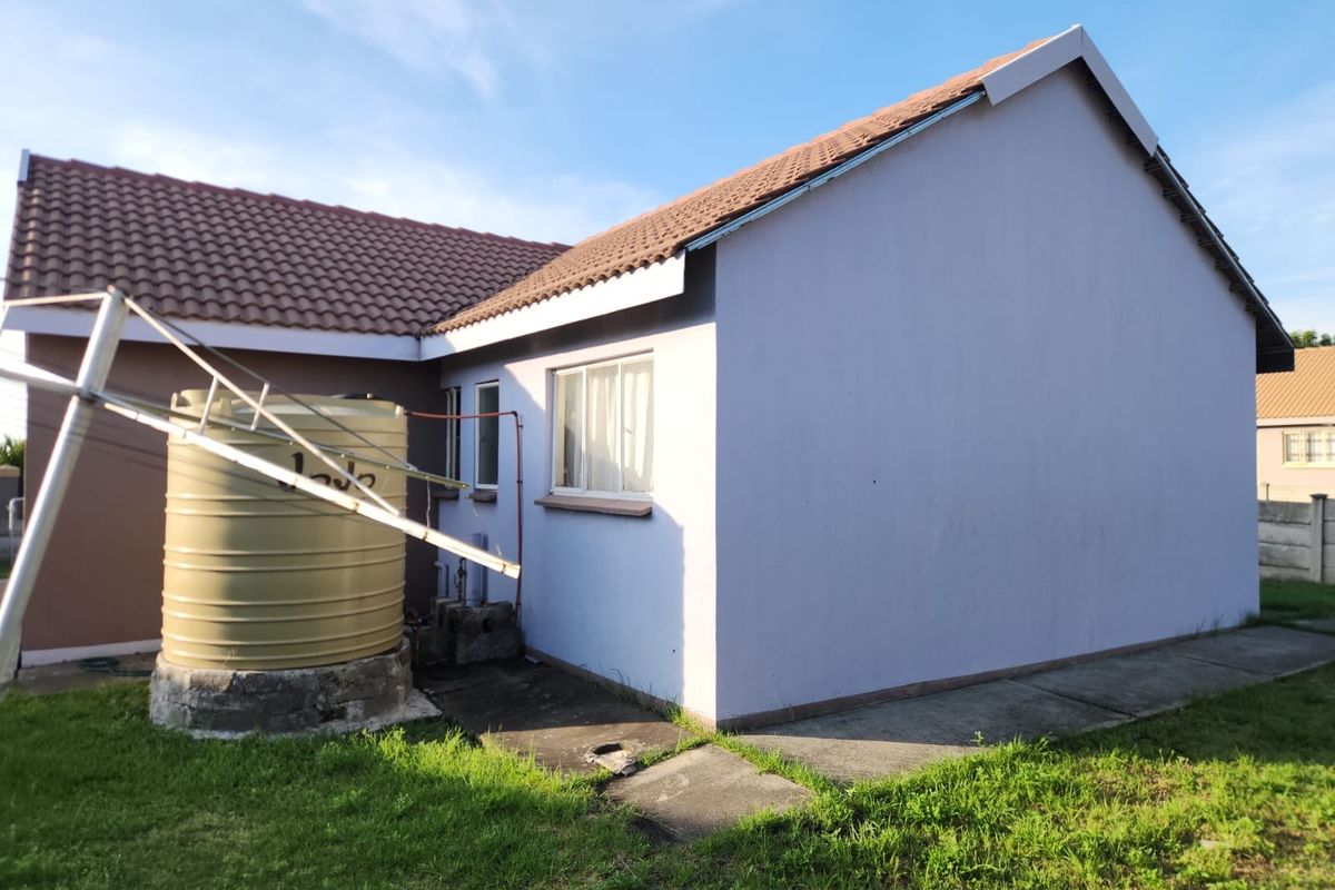 Rear exterior view of the property featuring a water storage tank, concrete pathway, and tiled roof structure.
