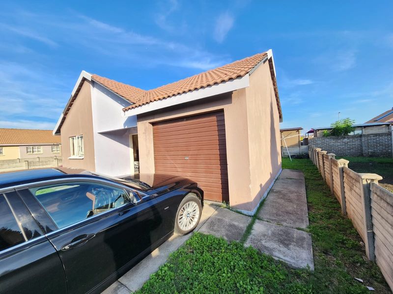 Front view of a single-story house featuring a brown garage door, tiled roof, and a concrete driveway with surrounding boundary wall.