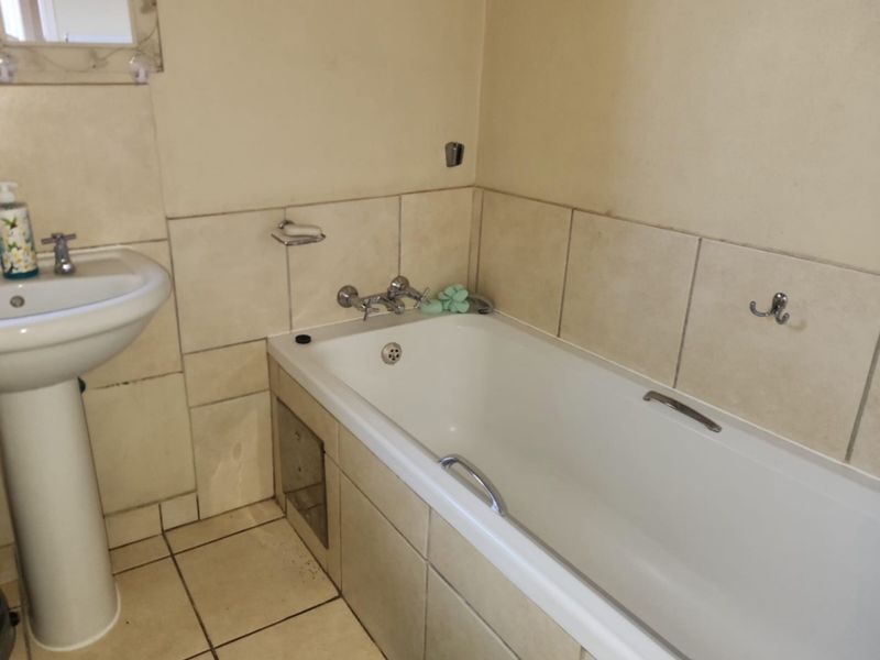 A functional bathroom featuring a pedestal basin and a built-in bathtub with chrome fixtures, finished with neutral ceramic wall and floor tiles.