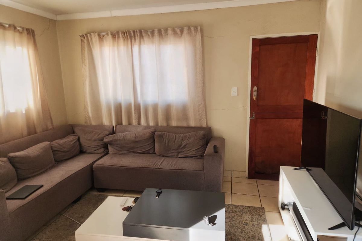 A living room featuring tiled flooring and a wooden door, showing signs of wear including visible wall cracks.