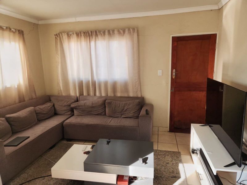 A living room featuring tiled flooring and a wooden door, showing signs of wear including visible wall cracks.