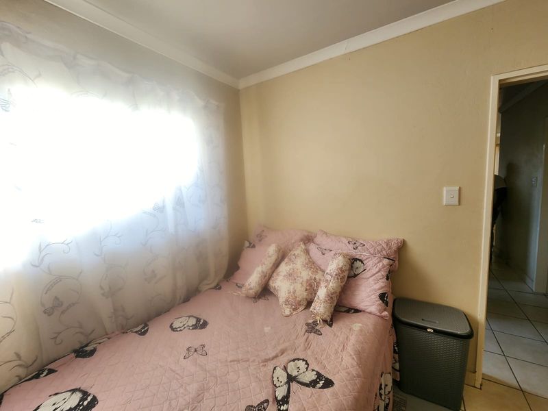 A compact bedroom featuring neutral wall finishes and a window with natural light, showing signs of wear on the ceiling cornice.