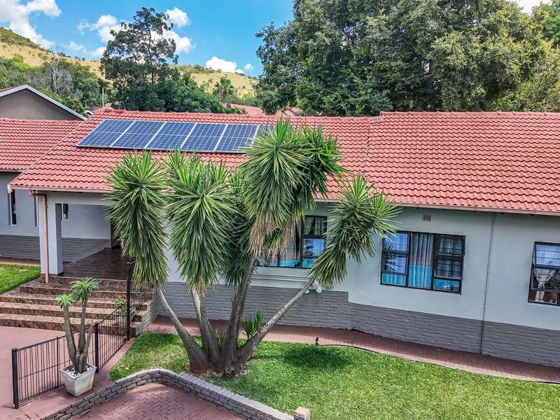 Front elevation of a residential house featuring a tiled roof with integrated solar panels, paved driveway, and landscaped garden area.