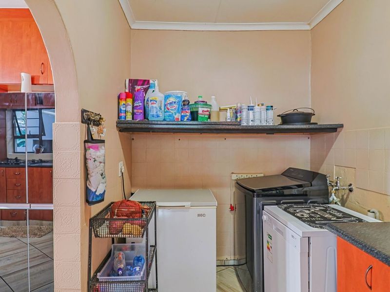 A functional laundry area featuring built-in cabinetry, laminate countertops, and tiled splashbacks, with direct access to the adjacent kitchen space.