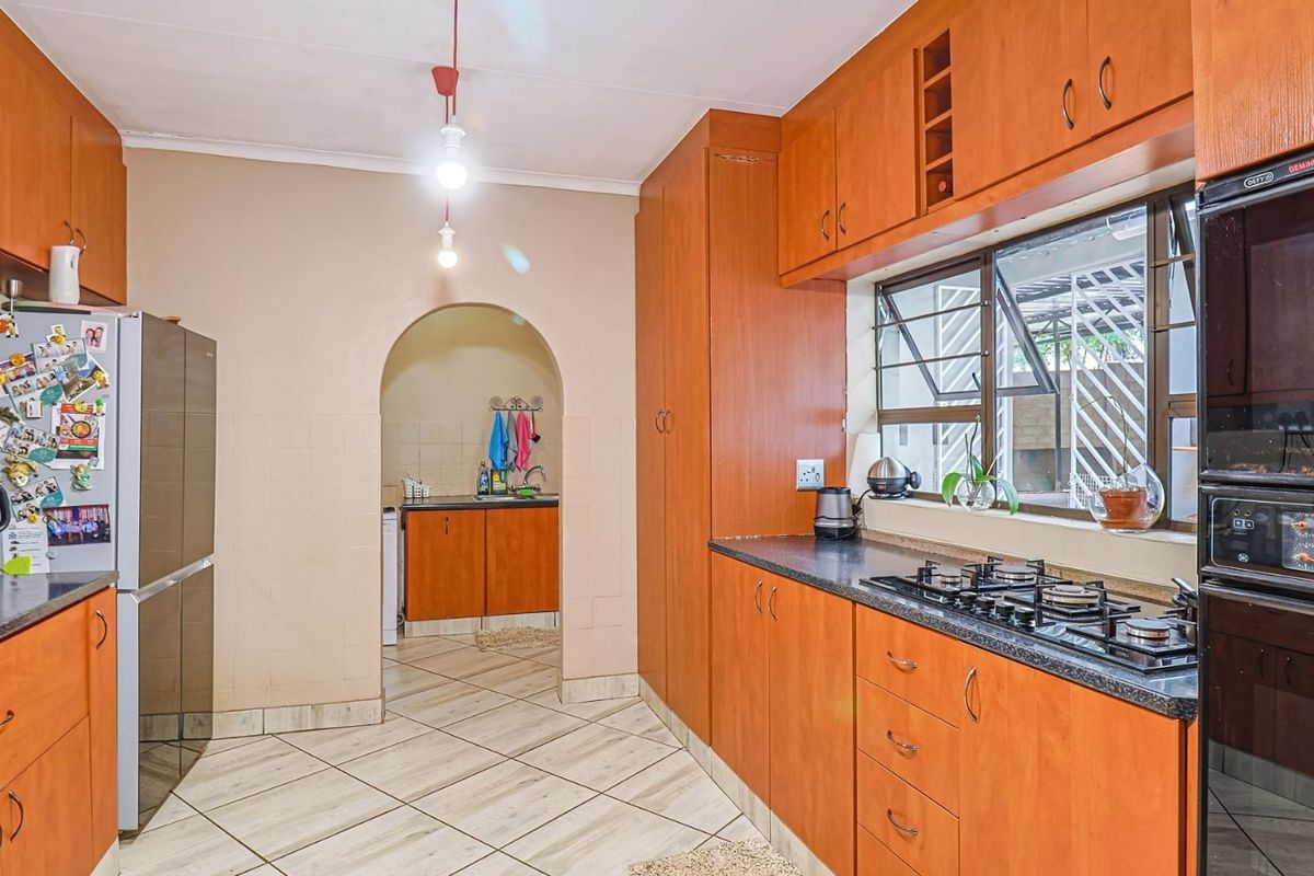 A functional kitchen featuring wooden cabinetry, a gas hob, built-in oven, and an adjoining scullery area accessible through a classic archway.