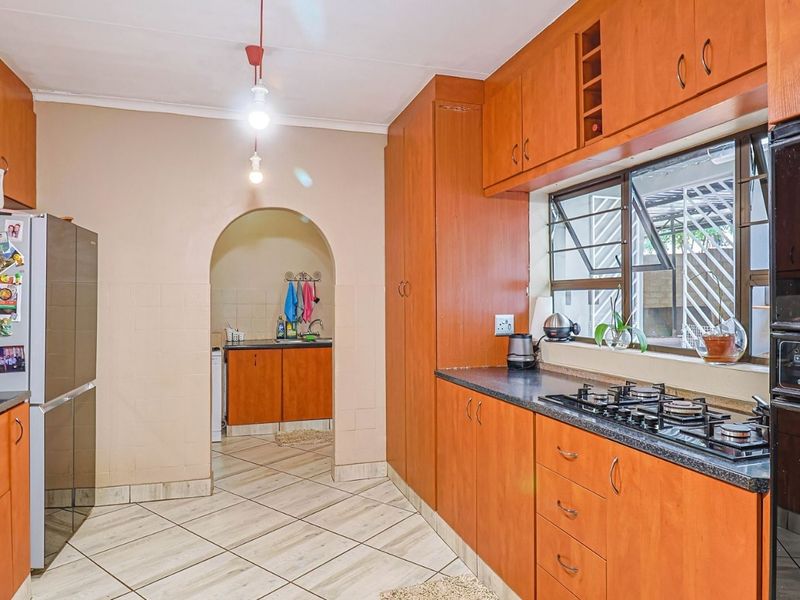 A functional kitchen featuring wooden cabinetry, a gas hob, built-in oven, and an adjoining scullery area accessible through a classic archway.