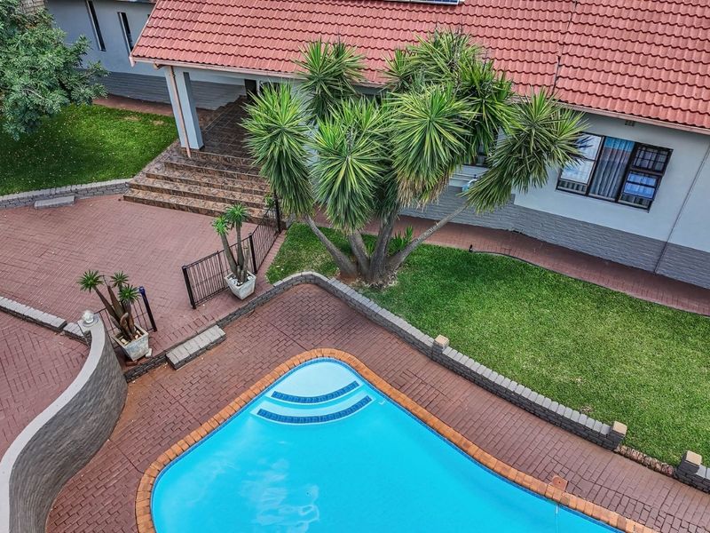 Aerial view of a well-maintained backyard featuring a swimming pool, paved patio area, landscaped lawn, and a tiled roof house exterior.