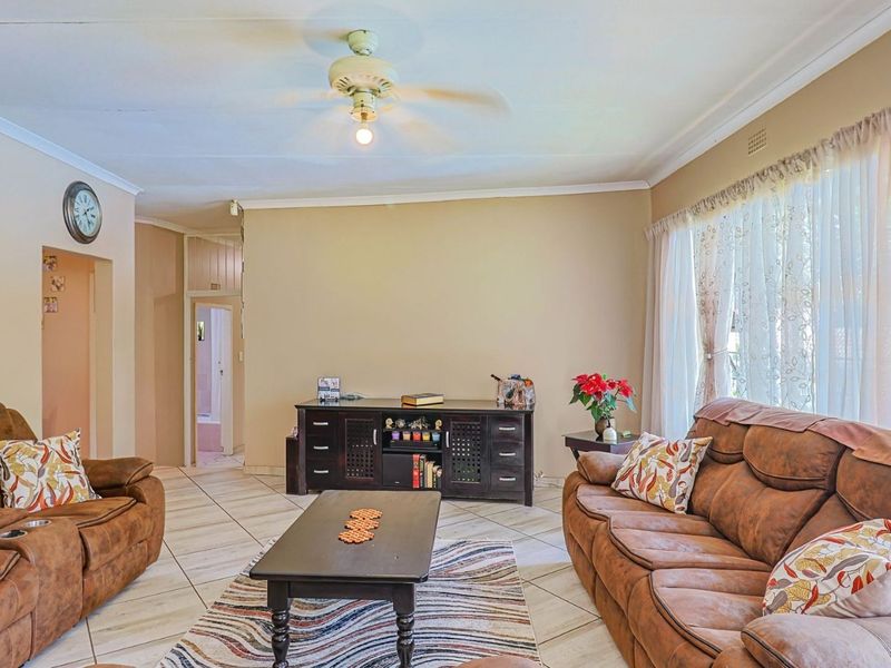 A spacious living room featuring tiled flooring, coved cornicing, and a central ceiling fan, offering a neutral base for interior updates.