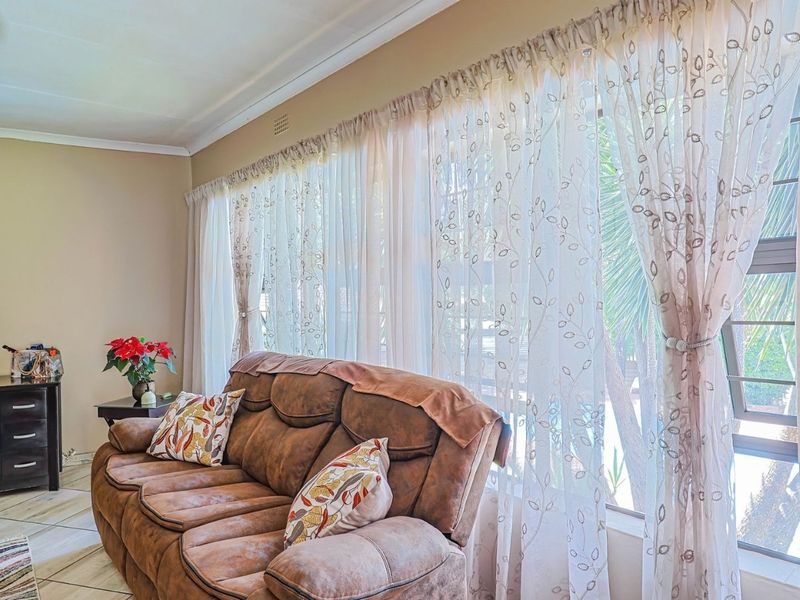 A bright living room featuring tiled flooring, a large window with natural light, and decorative cornice detailing.