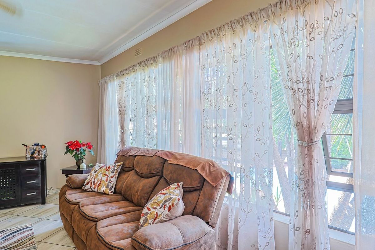 A bright living room featuring tiled flooring, a large window with natural light, and decorative cornice detailing.