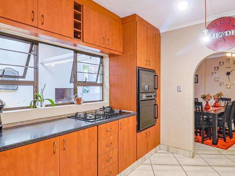Functional kitchen featuring warm-toned built-in cabinetry, a gas hob, and a built-in double oven, with an open archway leading to the dining area.
