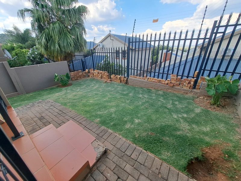 Rear garden area featuring a paved patio, lawn, and perimeter security fencing with unfinished brickwork and damaged step tiles.