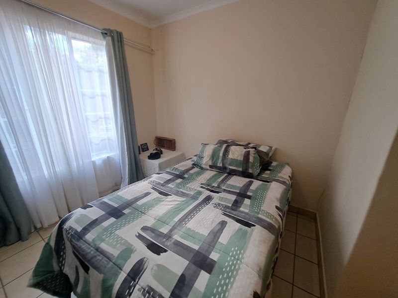 A compact bedroom featuring neutral wall finishes, tiled flooring, and a window with curtain treatments.