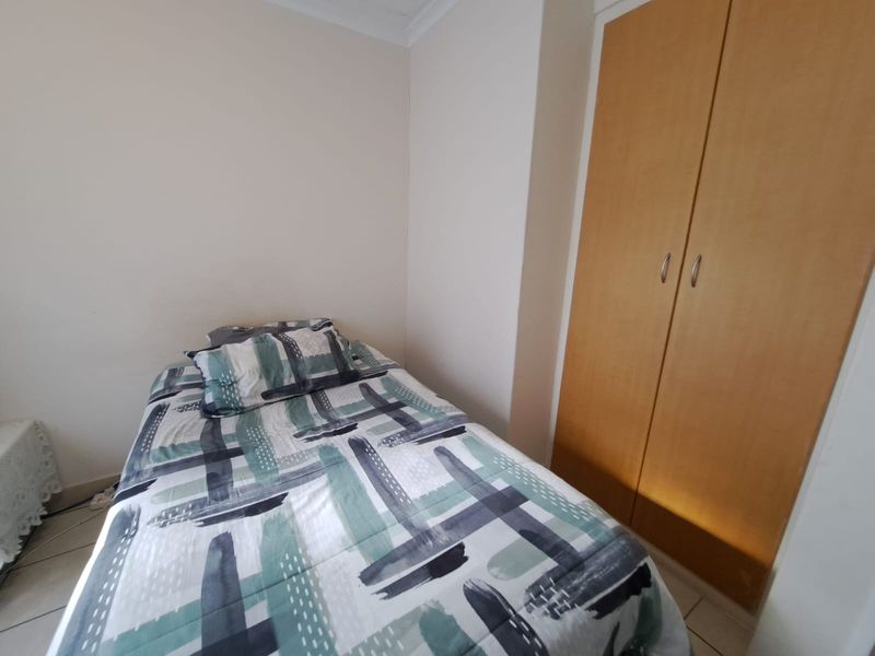 A functional bedroom featuring tiled flooring and a built-in wooden wardrobe, providing essential storage space.