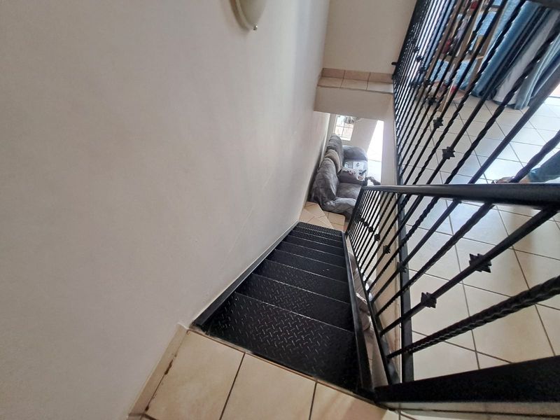 A view looking down a staircase featuring black metal treads and a decorative wrought iron balustrade with ceramic tiled flooring.