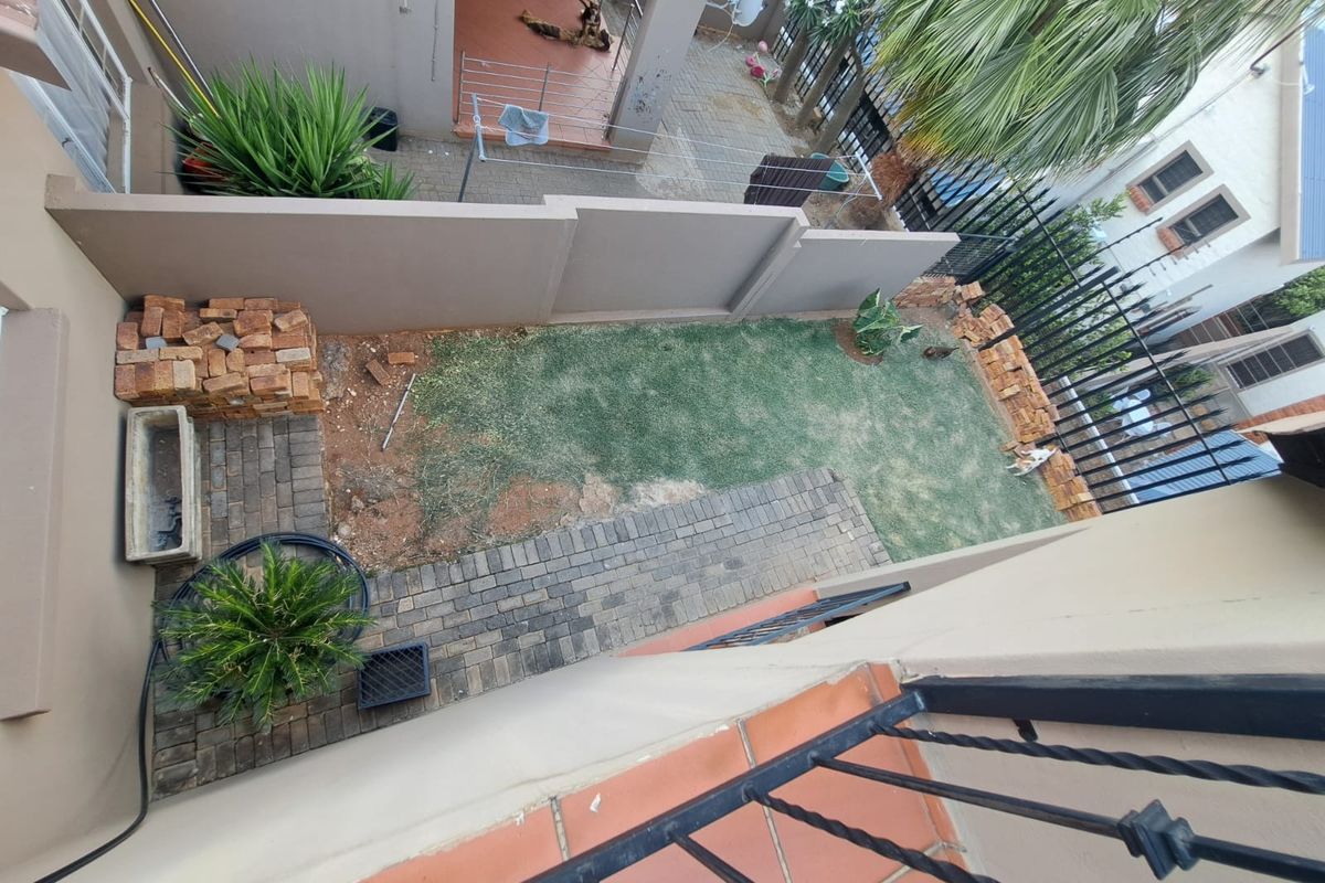 A rear courtyard area featuring a paved patio, a small lawn, and boundary walls with security fencing, requiring landscaping maintenance.