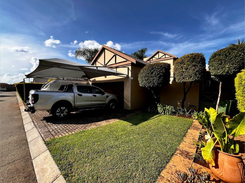Front exterior view of the townhouse featuring a paved driveway, shade sail carport, and well-maintained garden area.