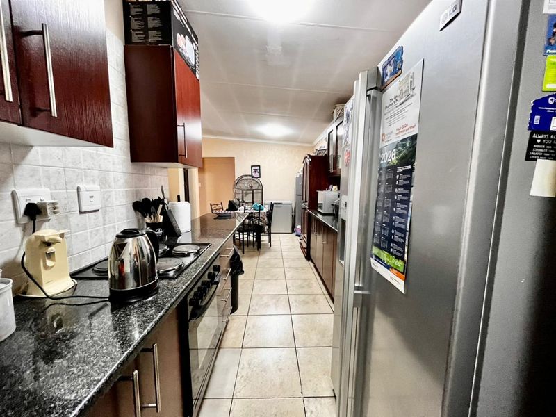 A functional galley-style kitchen featuring dark wood cabinetry, granite countertops, tiled flooring, and integrated cooking appliances.