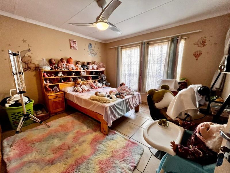 A bedroom featuring tiled flooring, a ceiling fan, and large windows with curtain rails, providing a functional space for rest.