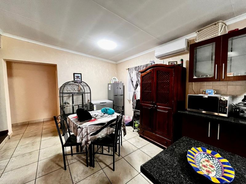 Open-plan kitchen and dining area featuring dark wood cabinetry, granite countertops, tiled flooring, and a wall-mounted air conditioning unit.