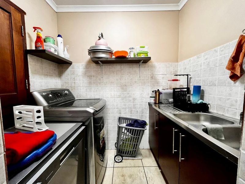 A functional laundry room featuring built-in dark cabinetry, a stainless steel sink, tiled splashback, and floating shelving for storage.