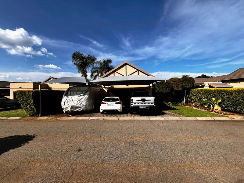 Front elevation of a townhouse featuring a paved driveway, double shade cloth carport, and well-maintained landscaped hedges.