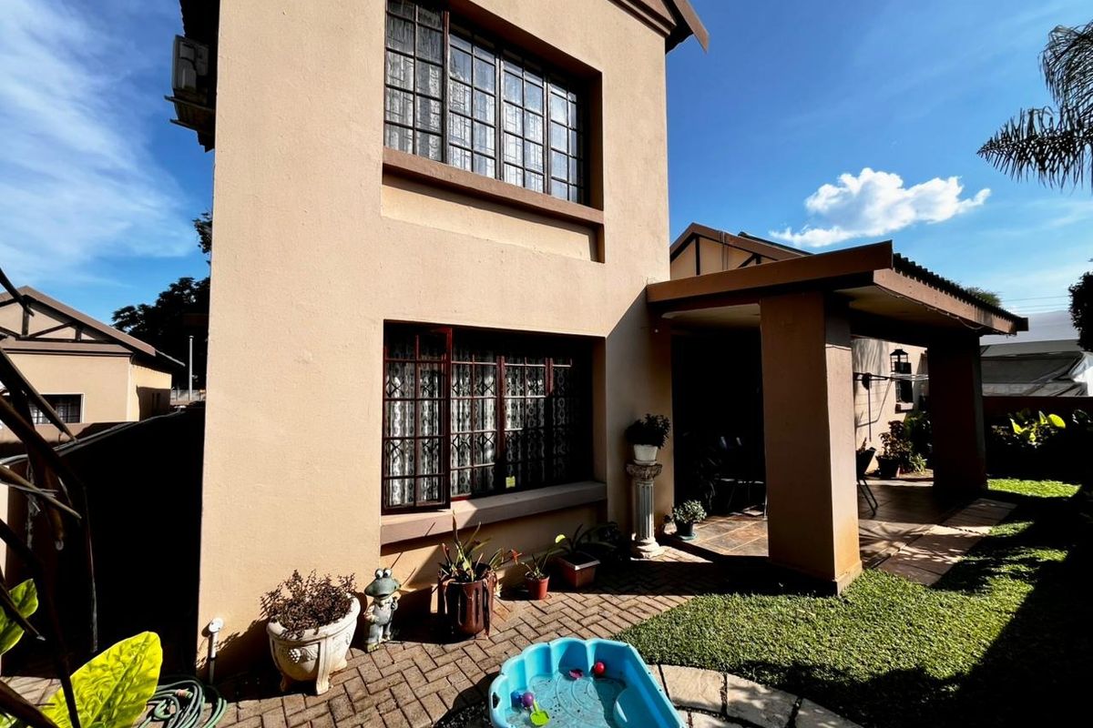 Rear view of the townhouse featuring a covered patio area, paved courtyard, and established garden space.