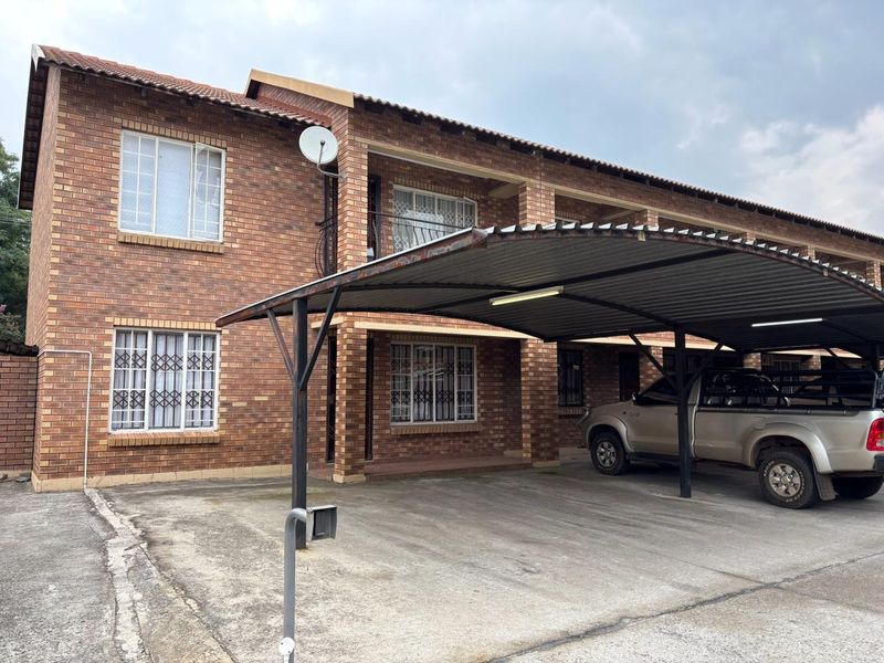 Exterior view of a face brick apartment building featuring a covered carport and secure window bars.