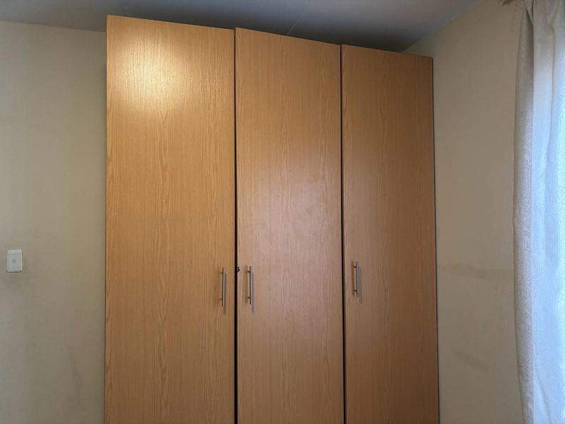 A bedroom featuring a functional, light wood-finish built-in wardrobe with modern metal handles.