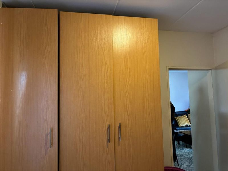 A bedroom featuring a large, light wood-finish built-in wardrobe with modern metal handles.