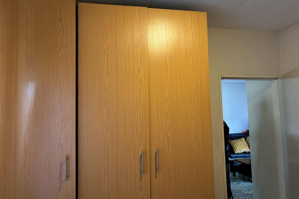 A bedroom featuring a large, light wood-finish built-in wardrobe with modern metal handles.