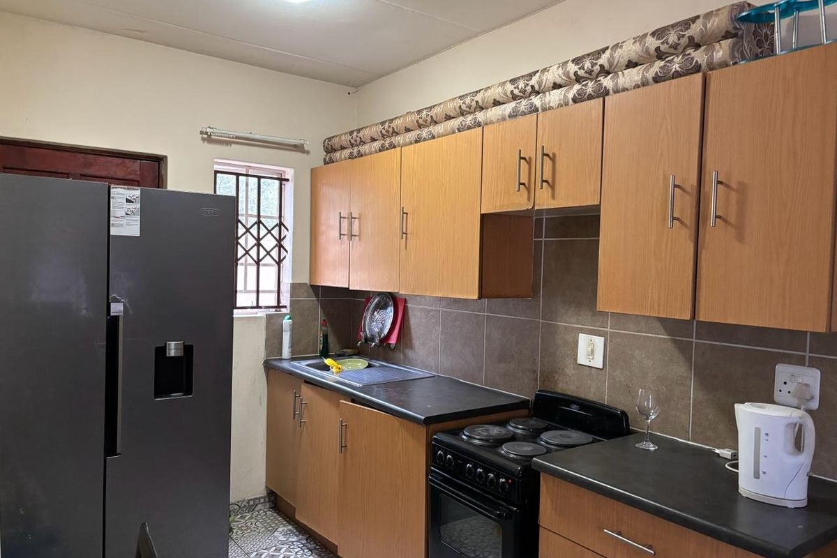 A functional kitchen featuring laminate cabinetry, dark countertops, a built-in oven with hob, and patterned floor tiles.