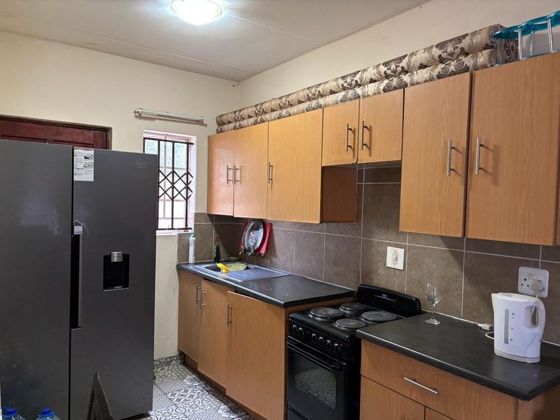 A functional kitchen featuring laminate cabinetry, dark countertops, a built-in oven with hob, and patterned floor tiles.