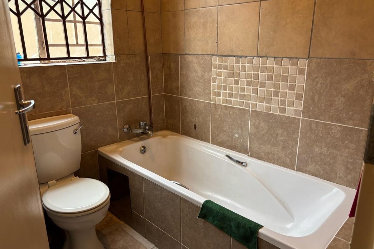 A functional bathroom featuring a bathtub, toilet, and neutral tiled finishes, complete with security bars on the window.