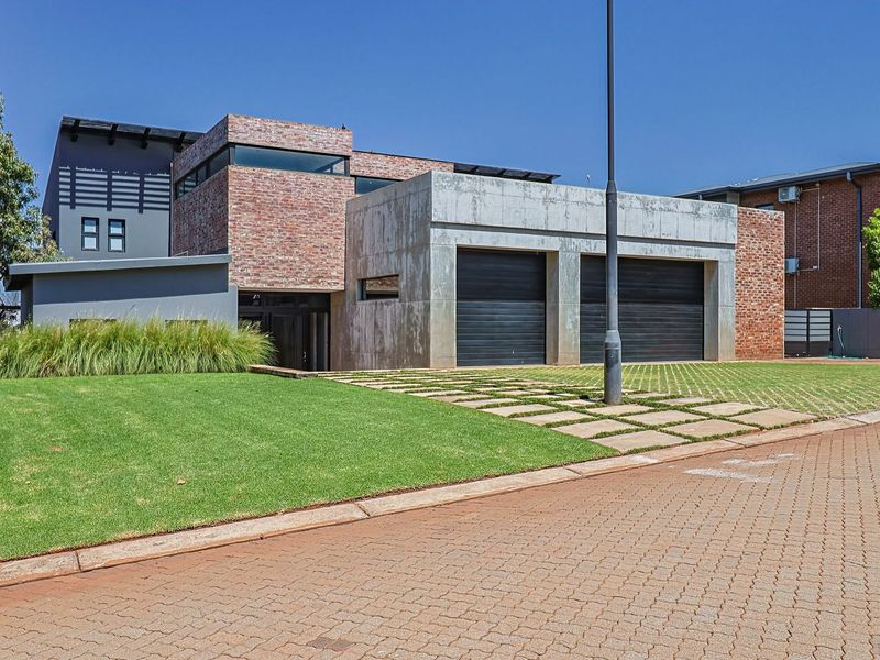Modern architectural house featuring a striking combination of exposed brick and concrete finishes with a double garage and well-maintained front lawn.