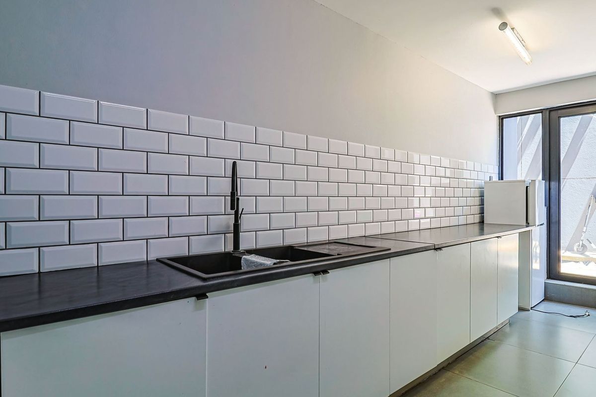 A clean, modern kitchen featuring white cabinetry, a black countertop, a subway tile backsplash, and a black sink with a matching mixer tap.