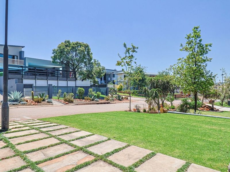 A well-maintained front exterior view featuring a paved driveway, landscaped garden, and stone paver walkway leading to the property entrance.